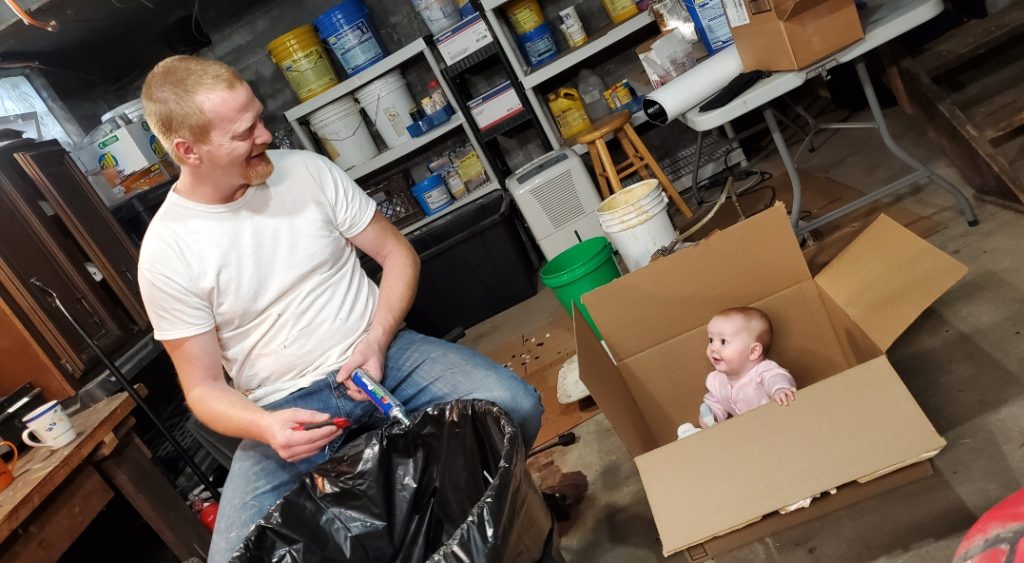 Steve Tolin prepares a squib rig tank in his home shop while his 6 month old daughter, Eloise, sits in a box and "helps."