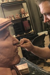 Bearded sculptor Kyle Roberst wears a Tolin FX t-shirt while adding detail to the larger than life-sized clay bust of August Wilson