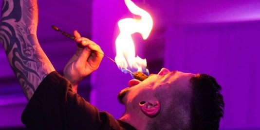 A tattooed young man holds a flame to his open mouth preparing to swallow it!